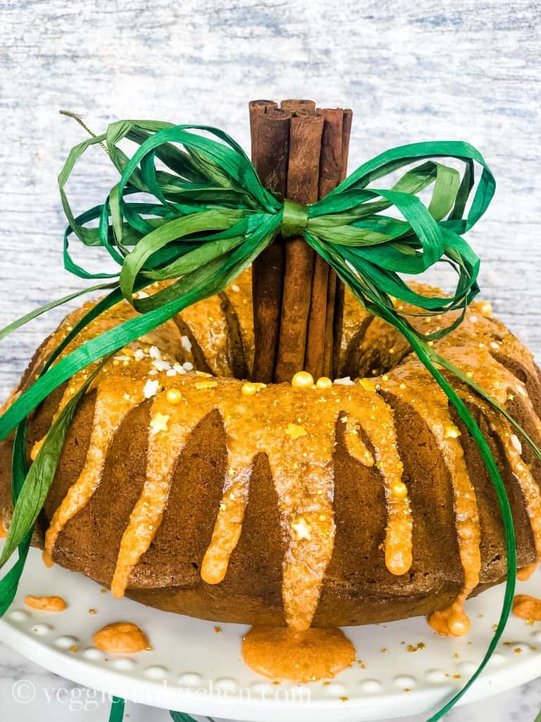 A round pumpkin cake with orange frosting and a green bow on top.