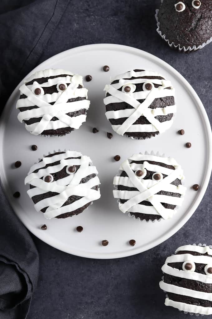 A plate of chocolate cupcakes with white icing to make them look like mummies.