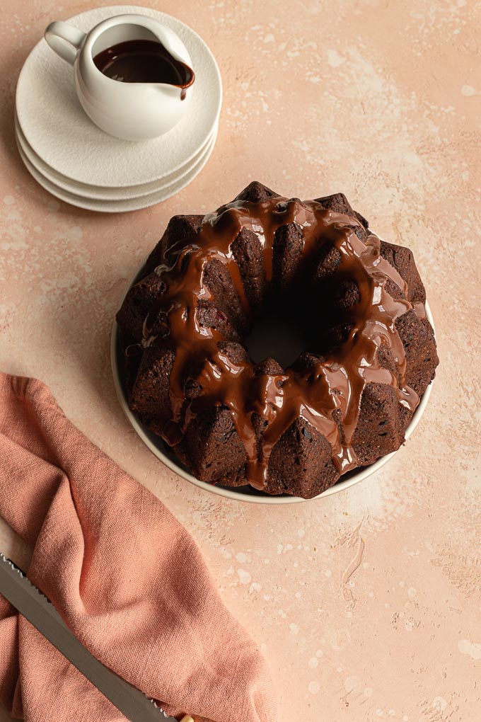A round chocolate cranberry cake with chocolate sauce on top.
