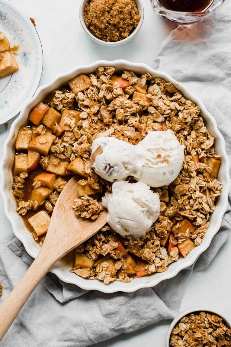 A dish of apple crisp topped with 3 scoops of ice cream.