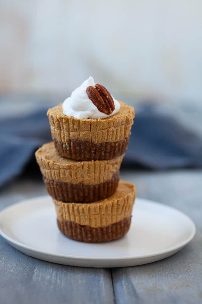 A stack of mini pumpkin cheesecakes topped with whipped cream and a pecan.