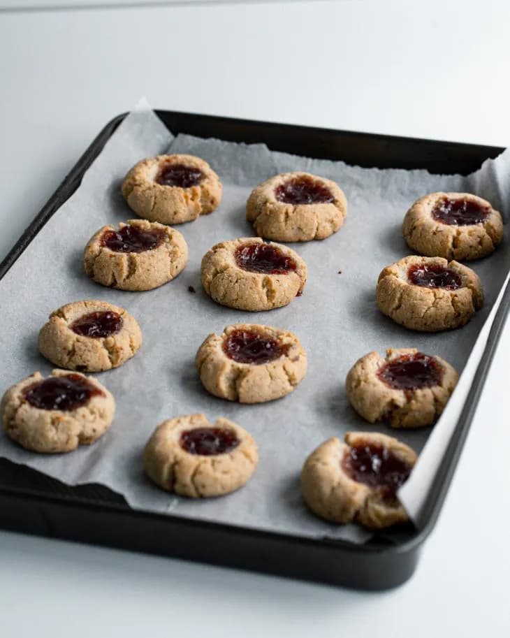 A baking pan of thumbprint cookies with jam in the middle.