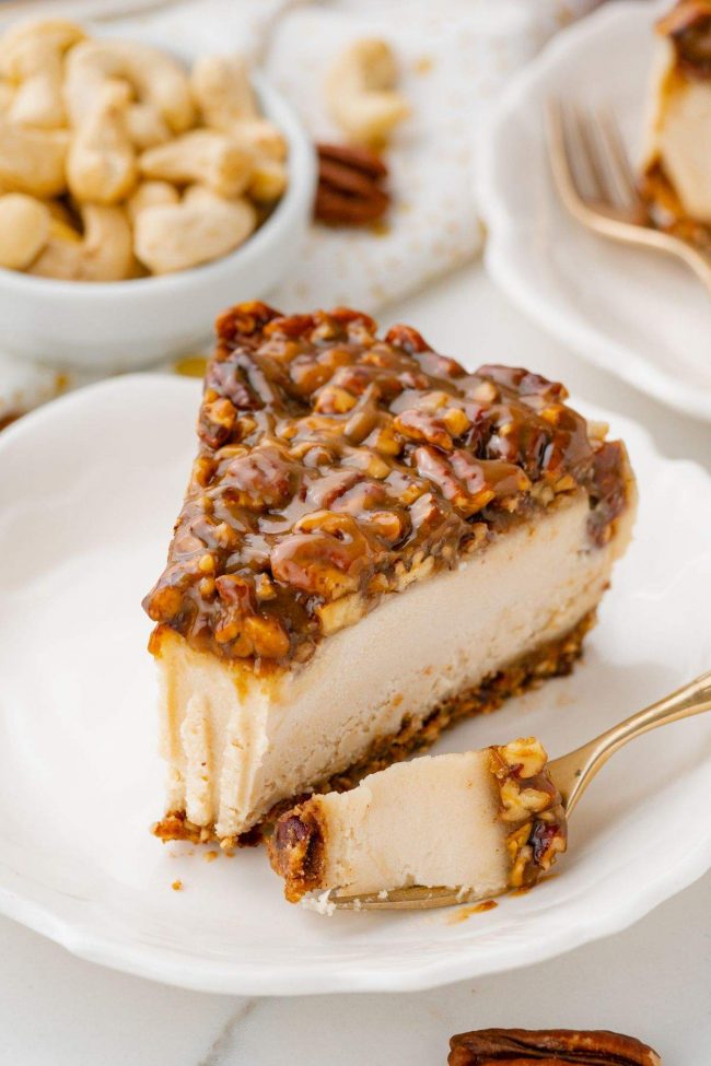 A thick slice of cheesecake topped with pecans and vegan caramel.