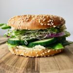 Side view of a bagel filled with vegan cream cheese, cucumber, onion, sprouts, and lettuce.