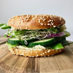 Side view of a bagel filled with vegan cream cheese, cucumber, onion, sprouts, and lettuce.