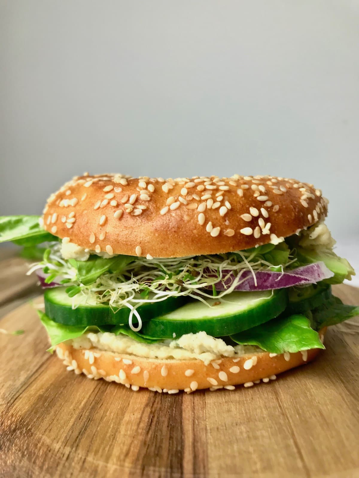 Side view of a bagel filled with vegan cream cheese, cucumber, onion, sprouts, and lettuce.