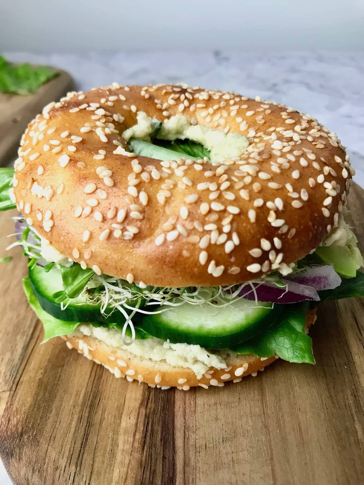 A bagel filled with vegan cream cheese, cucumber, onion, sprouts, and lettuce.