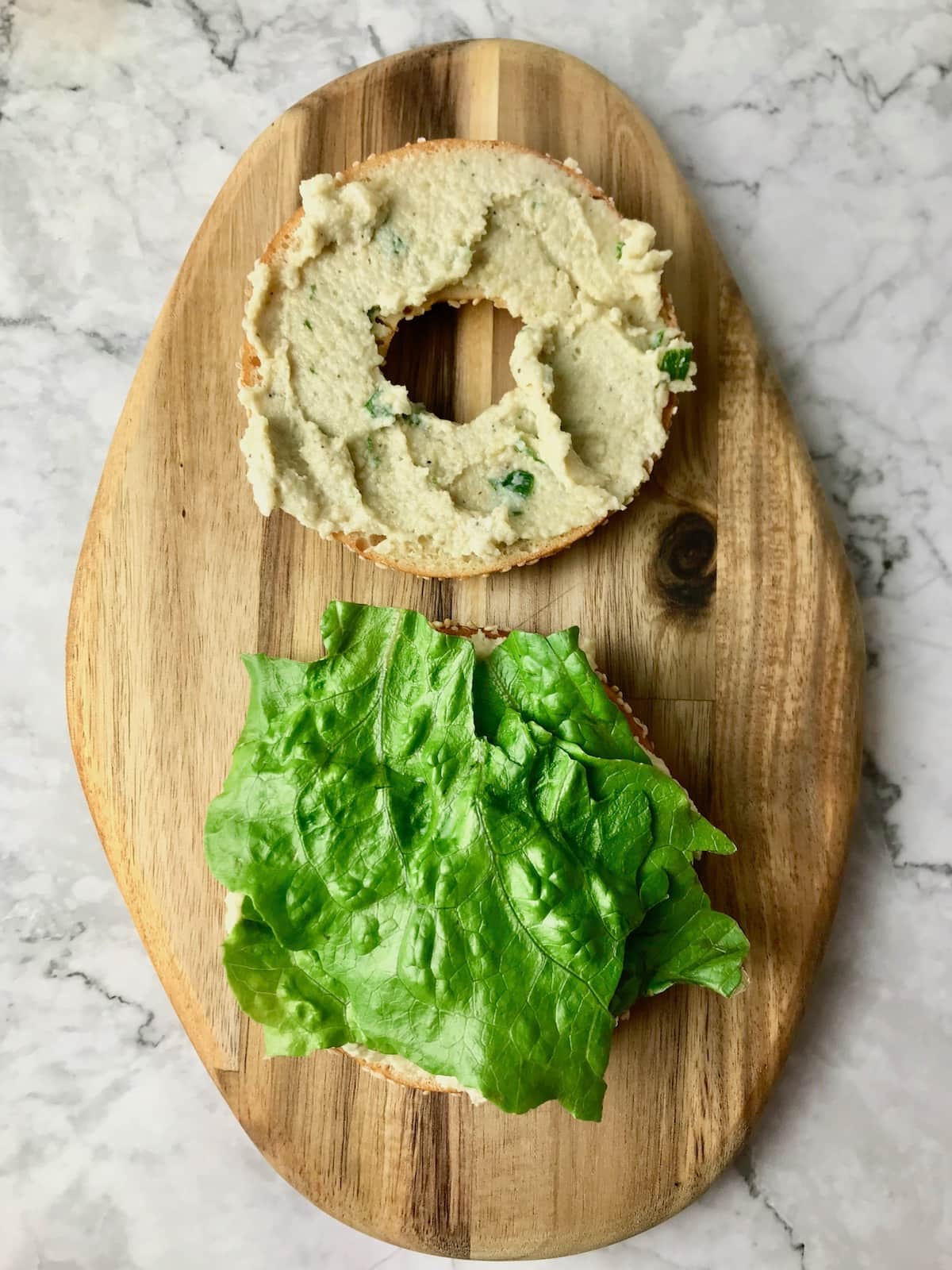 A bagel slice topped with cream cheese and another slice topped with lettuce.
