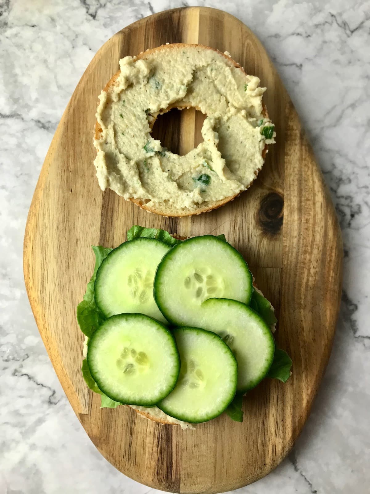 A bagel slice topped with cream cheese and another slice topped with lettuce and cucumber.