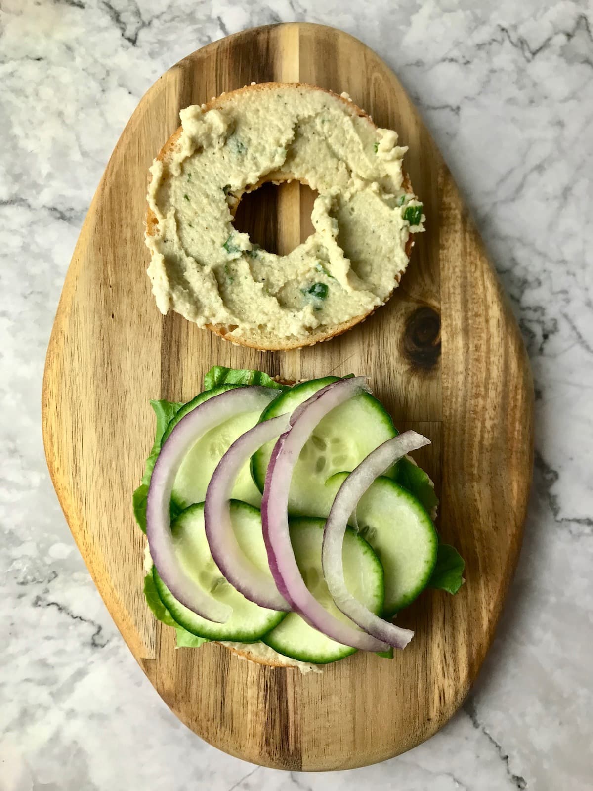 A bagel slice topped with cream cheese and another slice topped with lettuce, cucumber, and onion.
