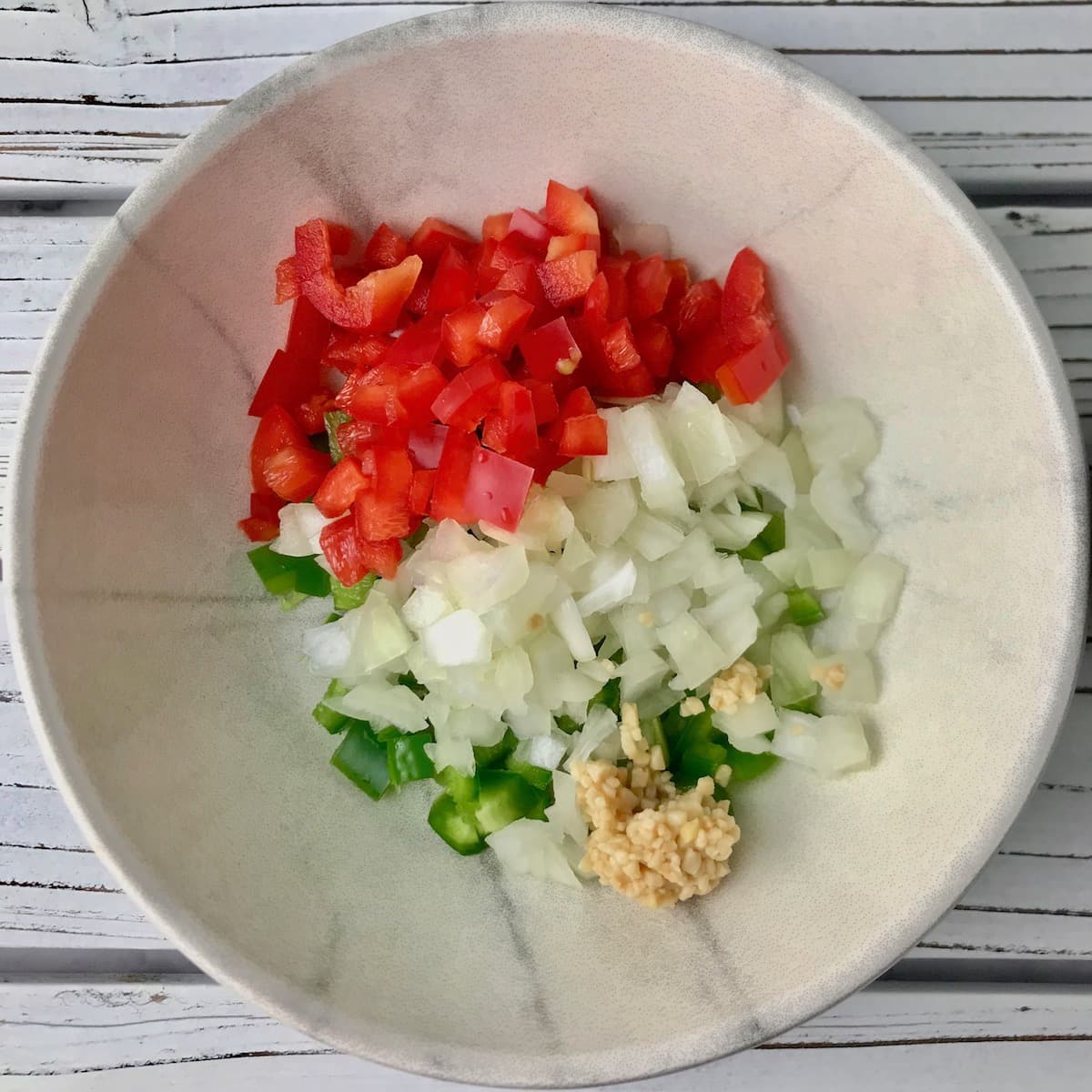 A bowl of chopped red pepper, onion, jalapeno pepper, and garlic.