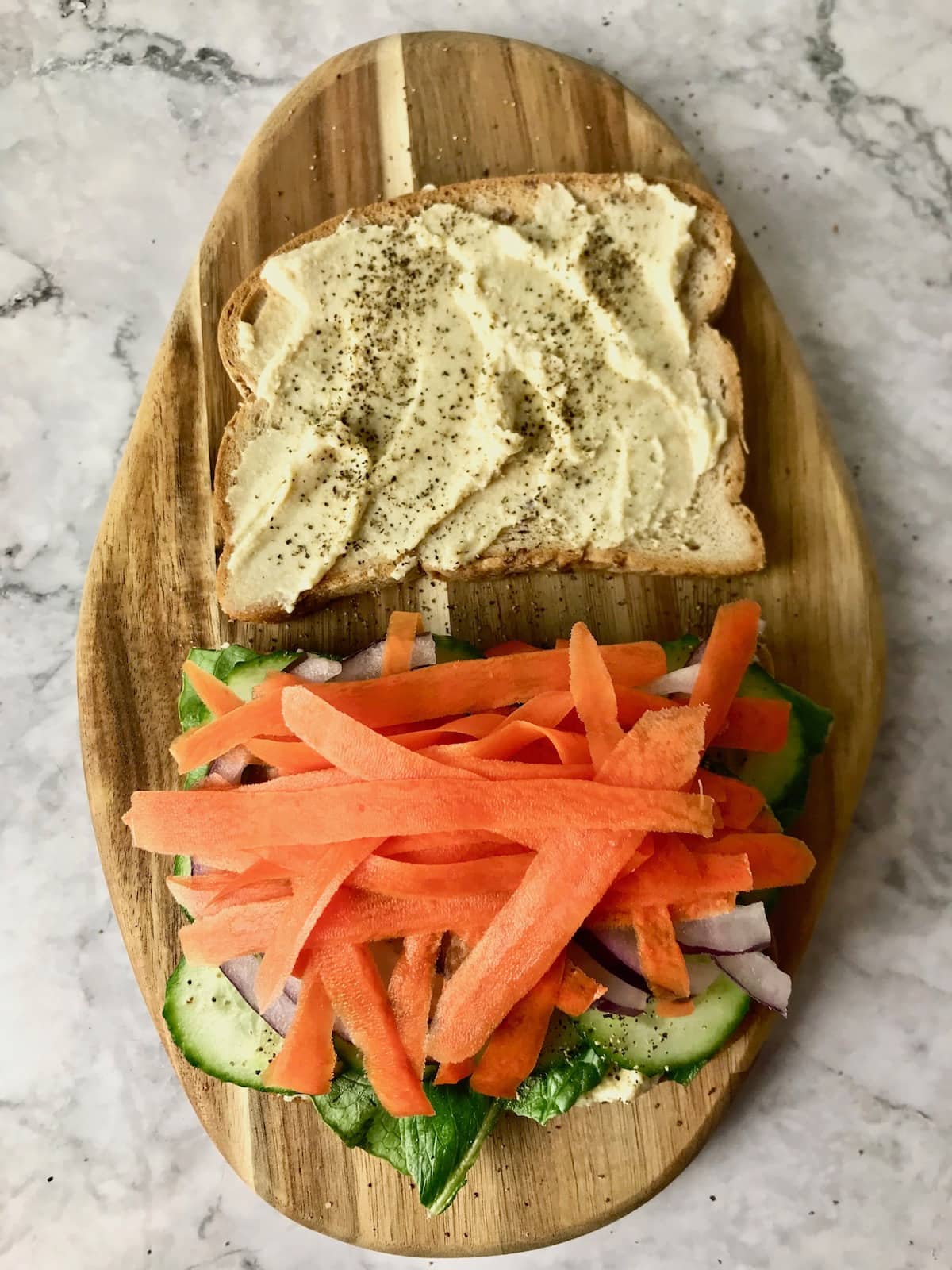 Two slices of bread, one topped with hummus, the other with various veggies including carrots on top.