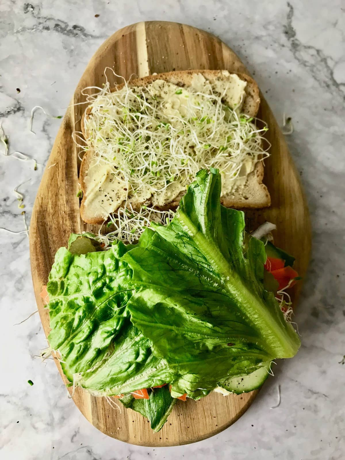 An open sandwich topped with hummus and various veggies, including lettuce and sprouts.