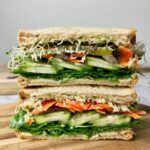 Two sandwich halves stacked on each other, showing them filled with pickles, carrot, onion, sprouts, and cucumber.