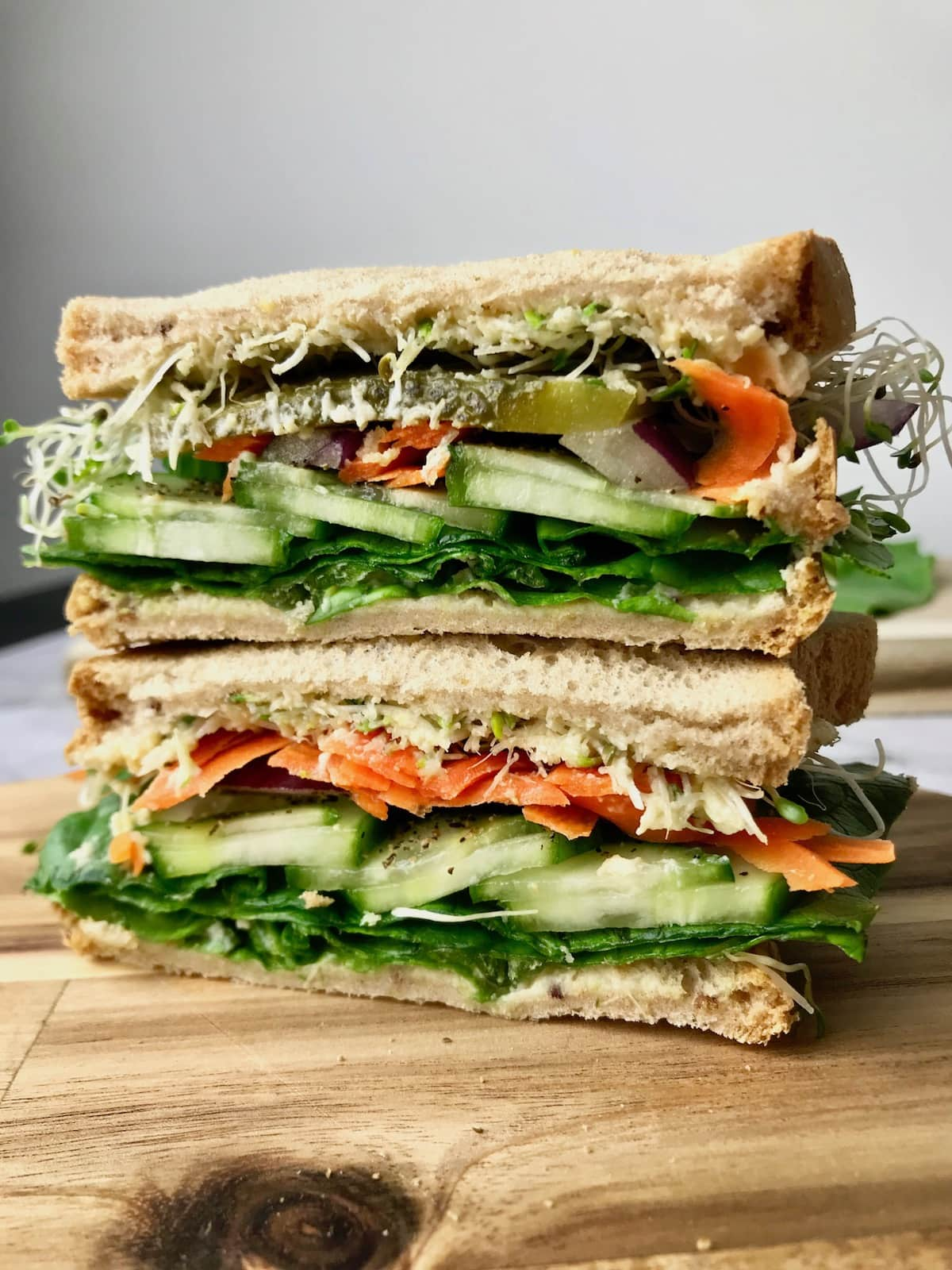 Two sandwich halves stacked on each other, showing them filled with pickles, carrot, onion, sprouts, and cucumber.