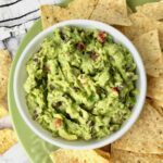 A bowl of black bean guacamole on a plate with tortilla chips.