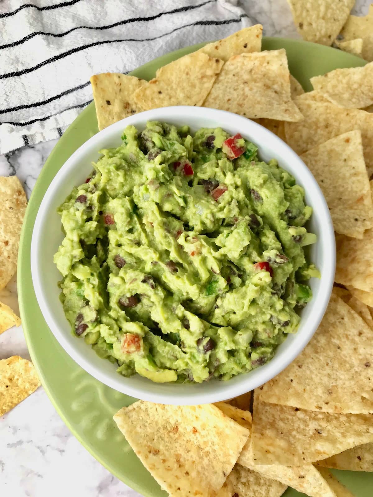 A bowl of black bean guacamole on a plate with tortilla chips.