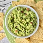 A bowl of guacamole on a plate of chips.