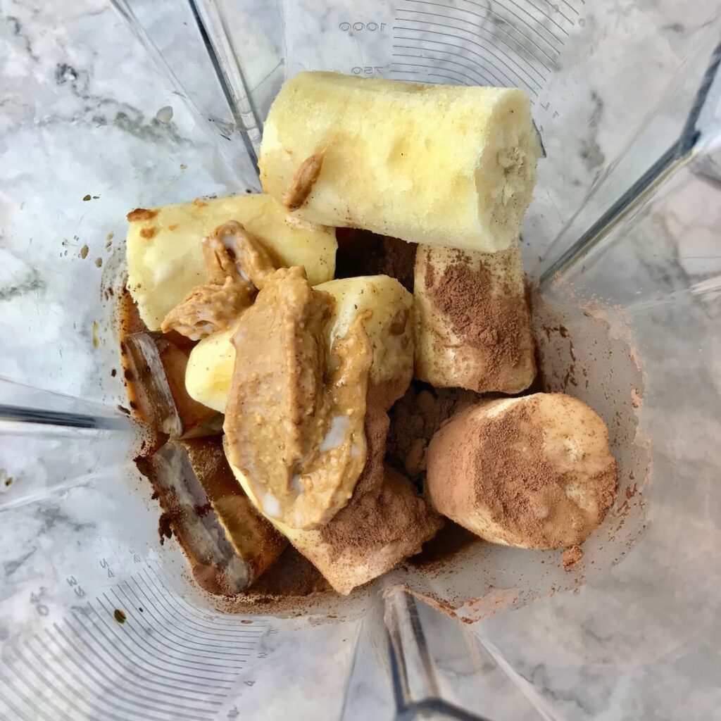 Frozen banana, frozen coffee cubes, cocoa powder, and peanut butter in a blender.