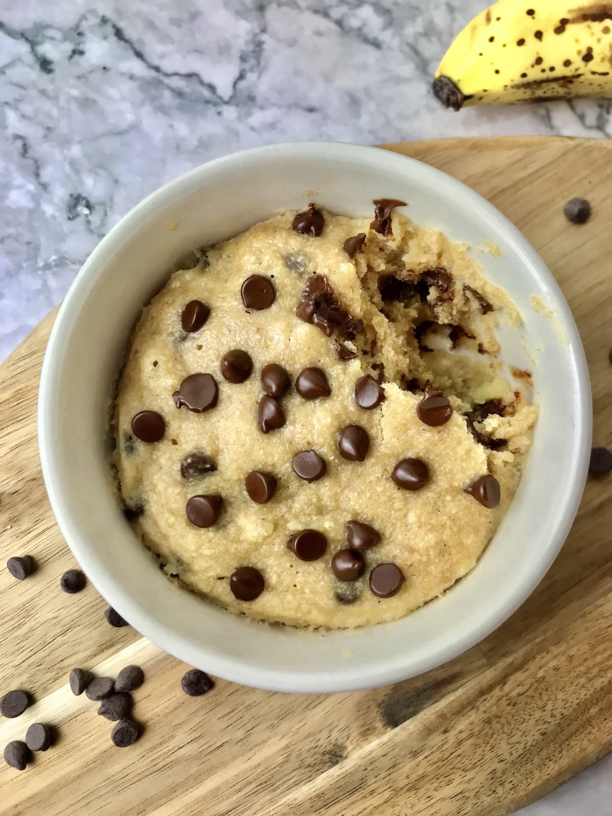 A banana mug cake topped with chocolate chips with a bite missing.