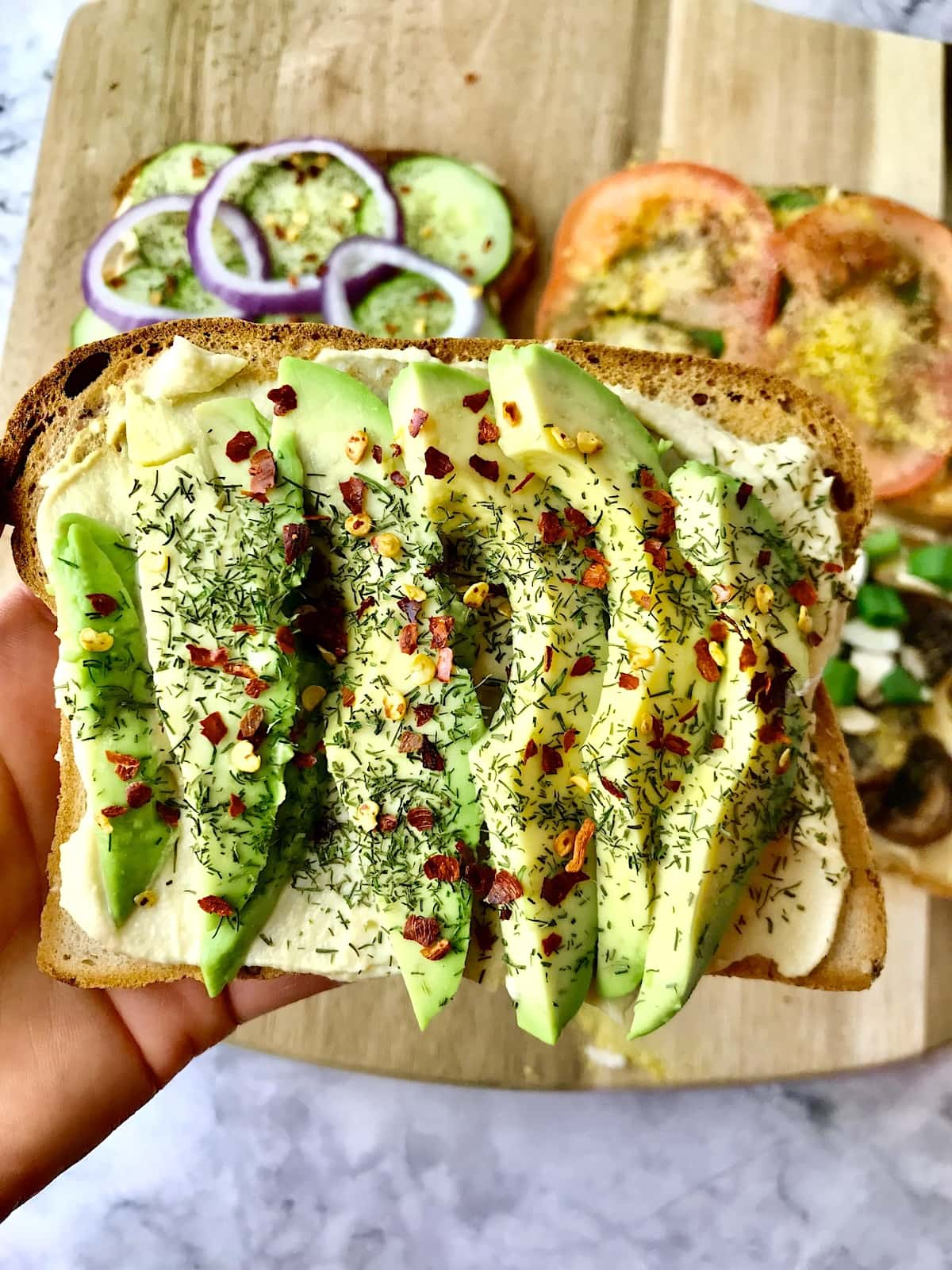 A piece of hummus toast topped with sliced avocado and crushed red pepper.