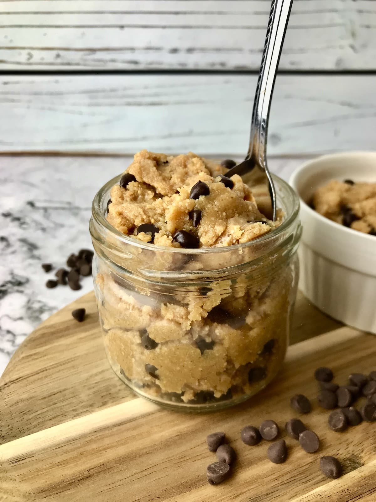 A mason jar filled with peanut butter cookie dough with chocolate chips next to it.