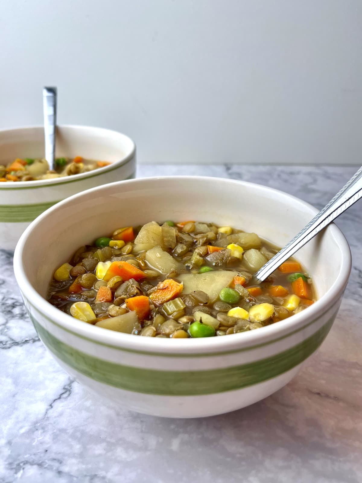 Two bowls of vegan lentil potato stew with spoons in them.