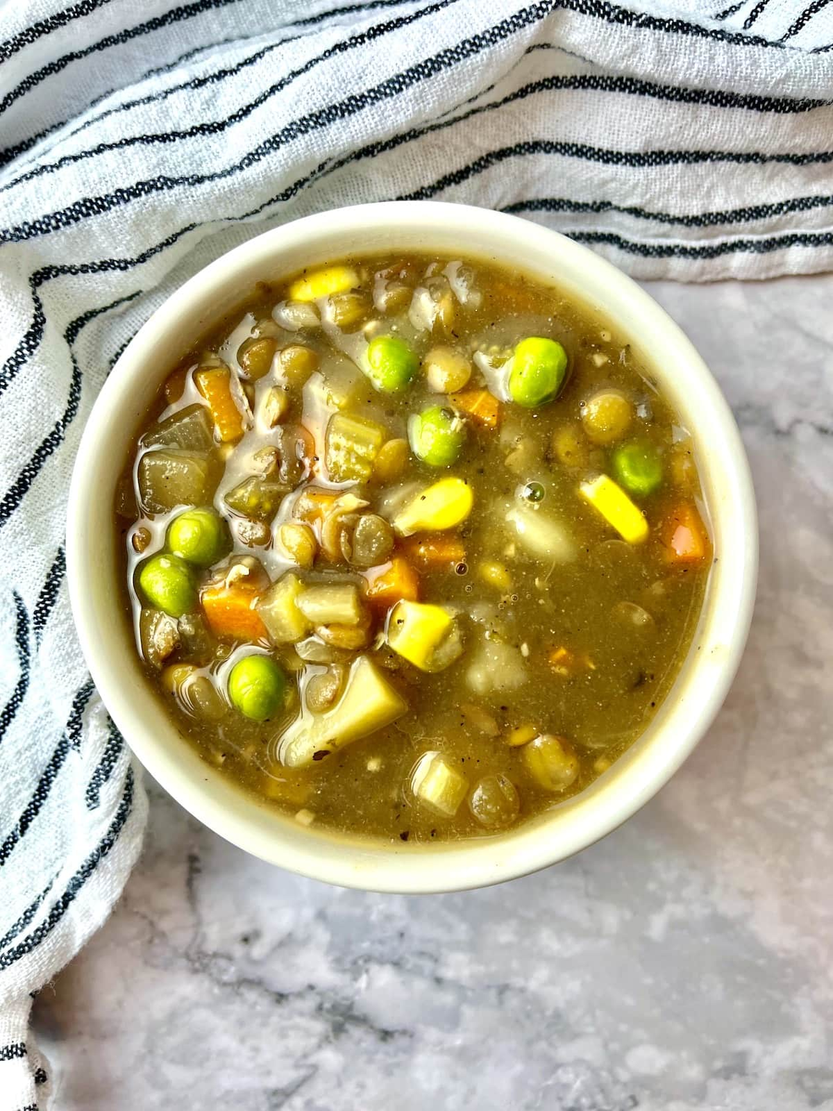 A bowl of lentil stew with peas, corn, carrot, potatoes, and lentils.