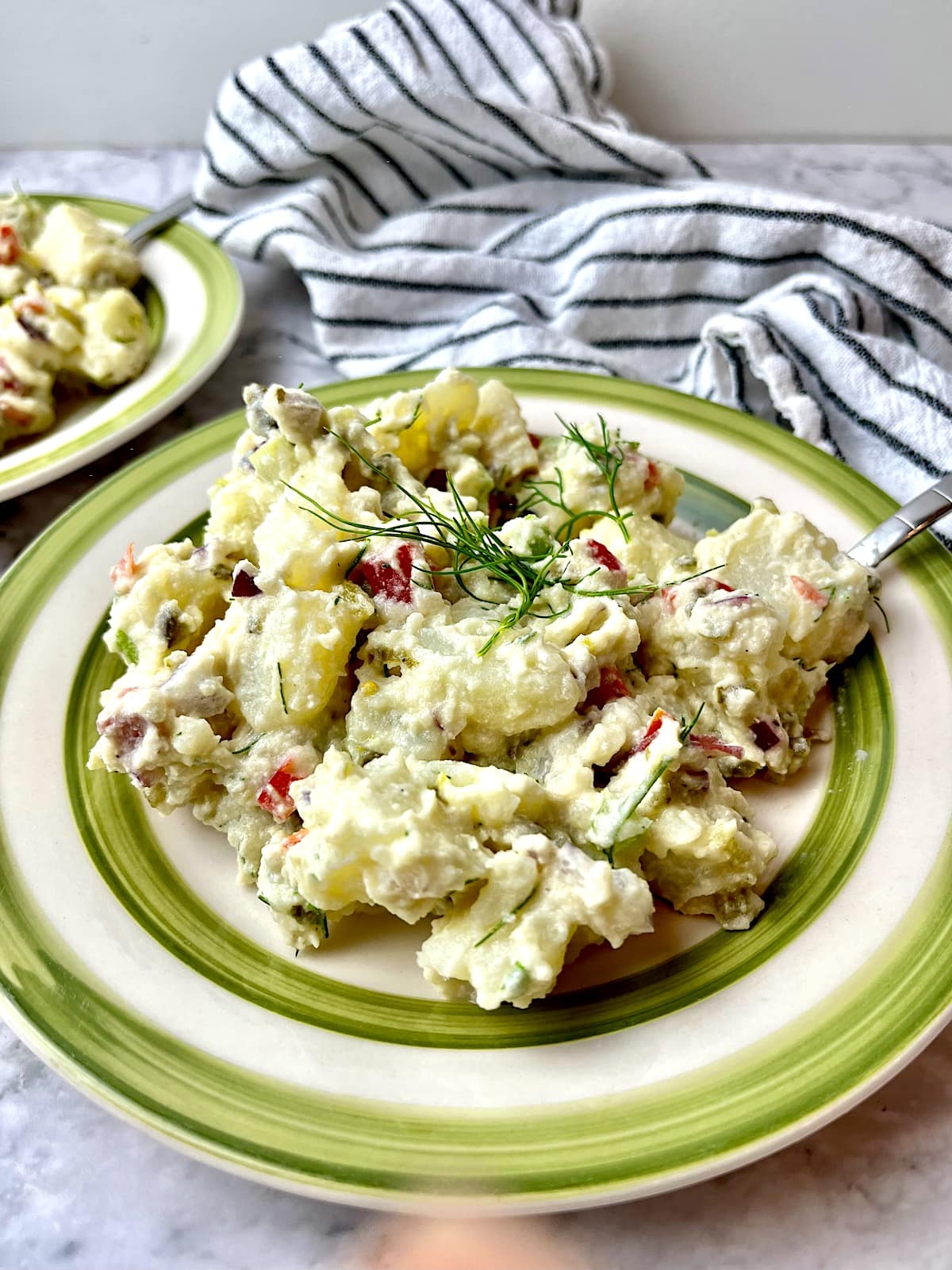 Vegan potato salad topped with fresh dill next to a dish towel.