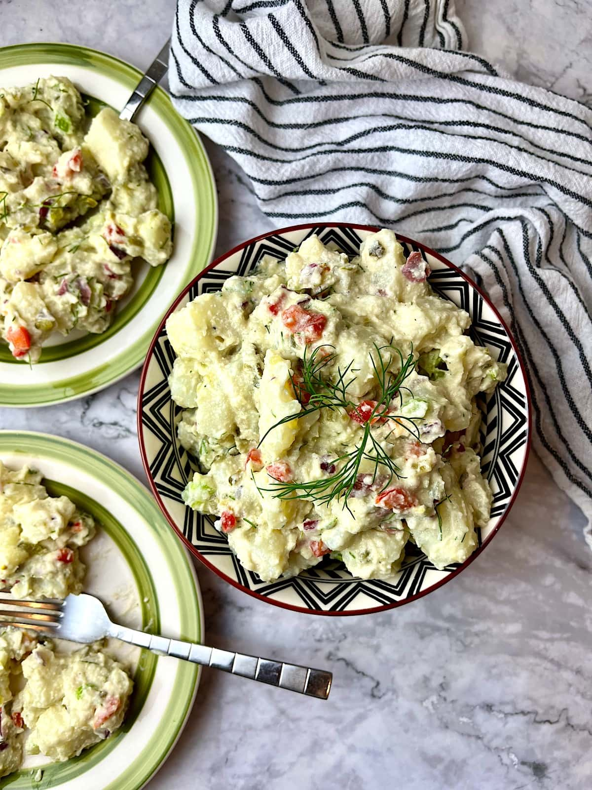 A bowl of vegan potato salad next to two plates of potato salad.