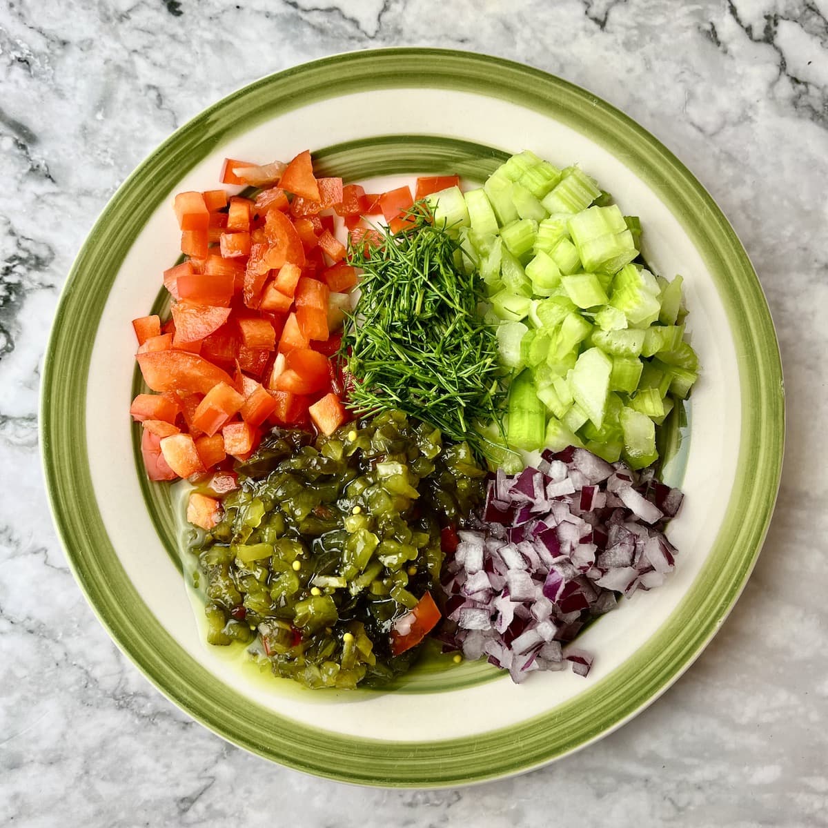 A plate of chopped red pepper, celery, red onion, relish, and dill. 