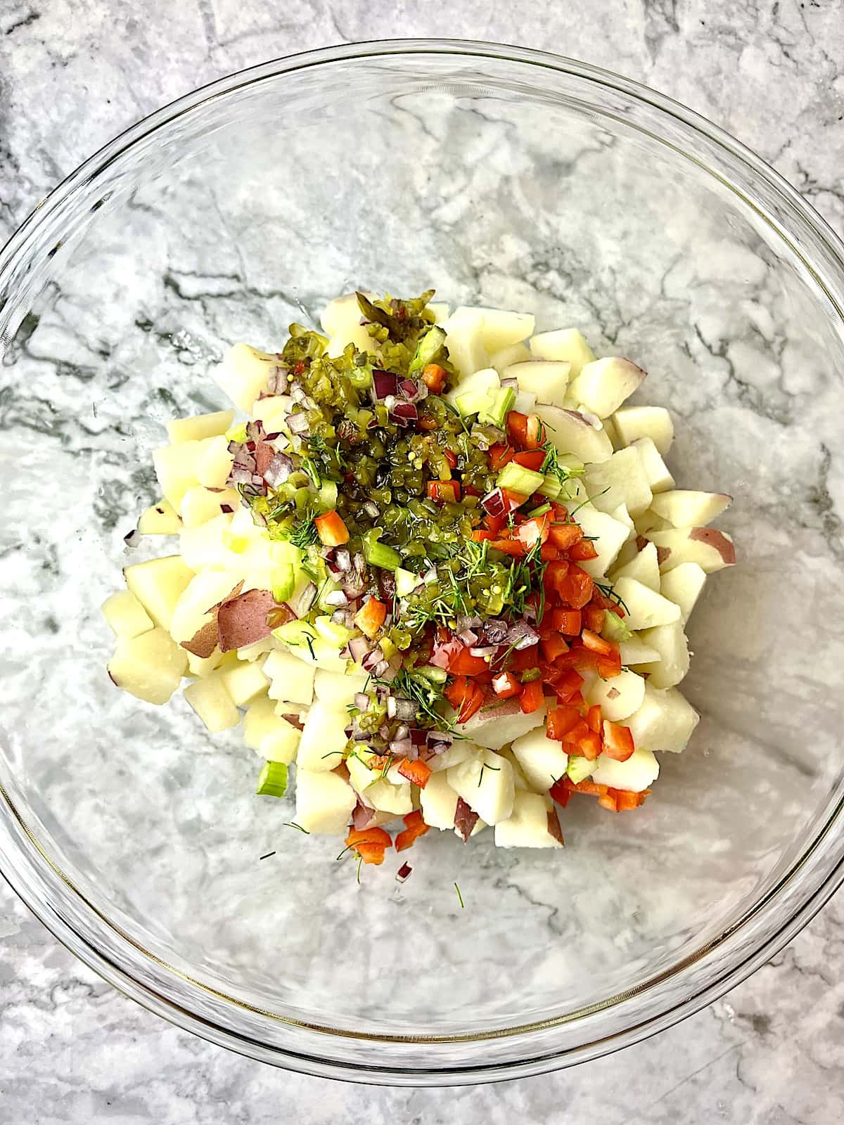 Potato salad ingredients in a clear glass bowl.