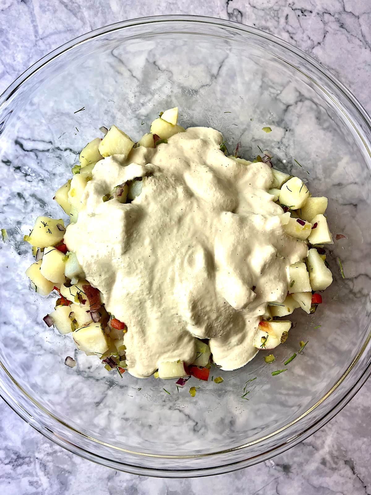 A bowl of potato salad ingredients with a creamy cashew dressing poured on top.