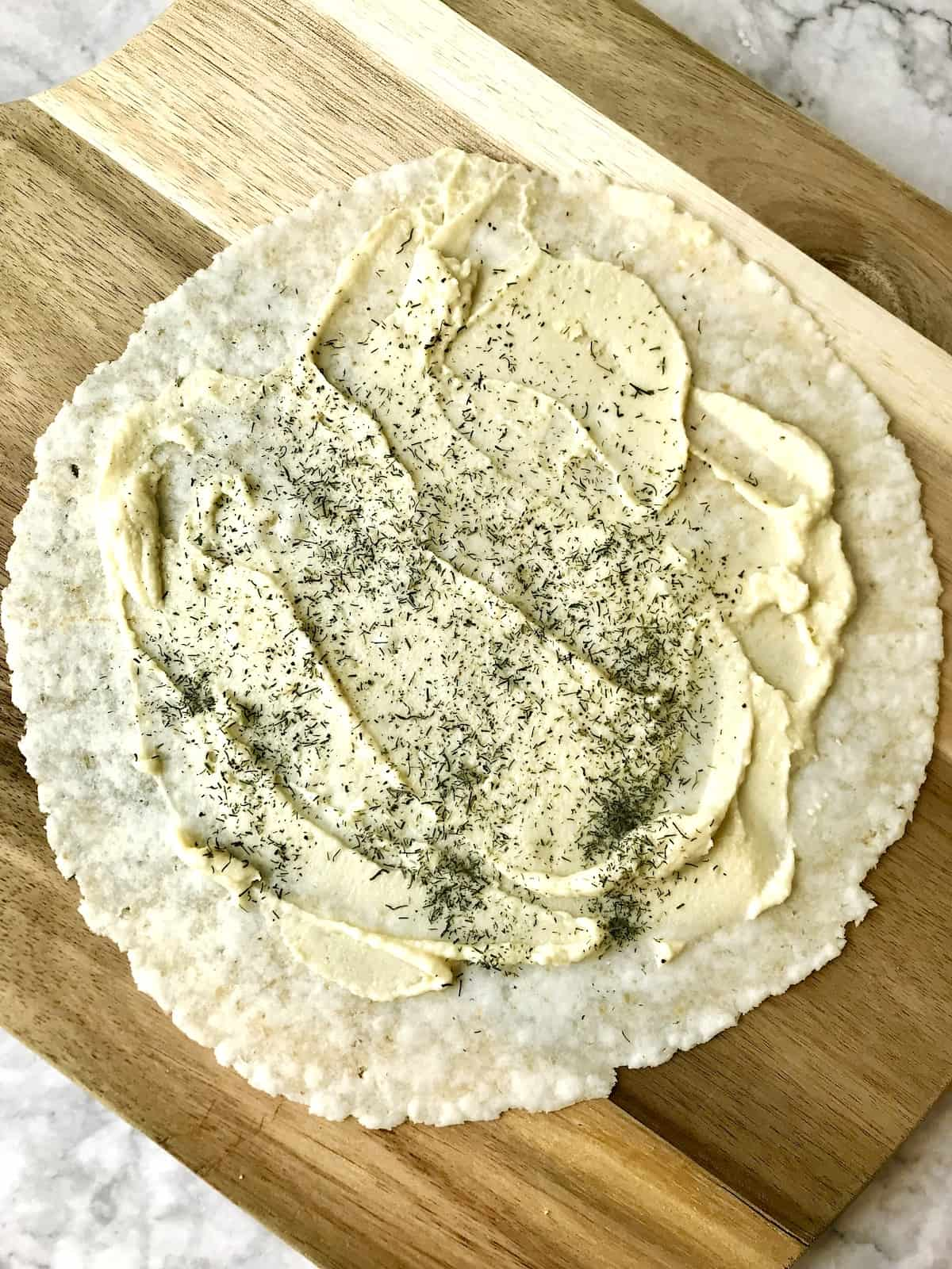 A tortilla with hummus and dried dill on it.