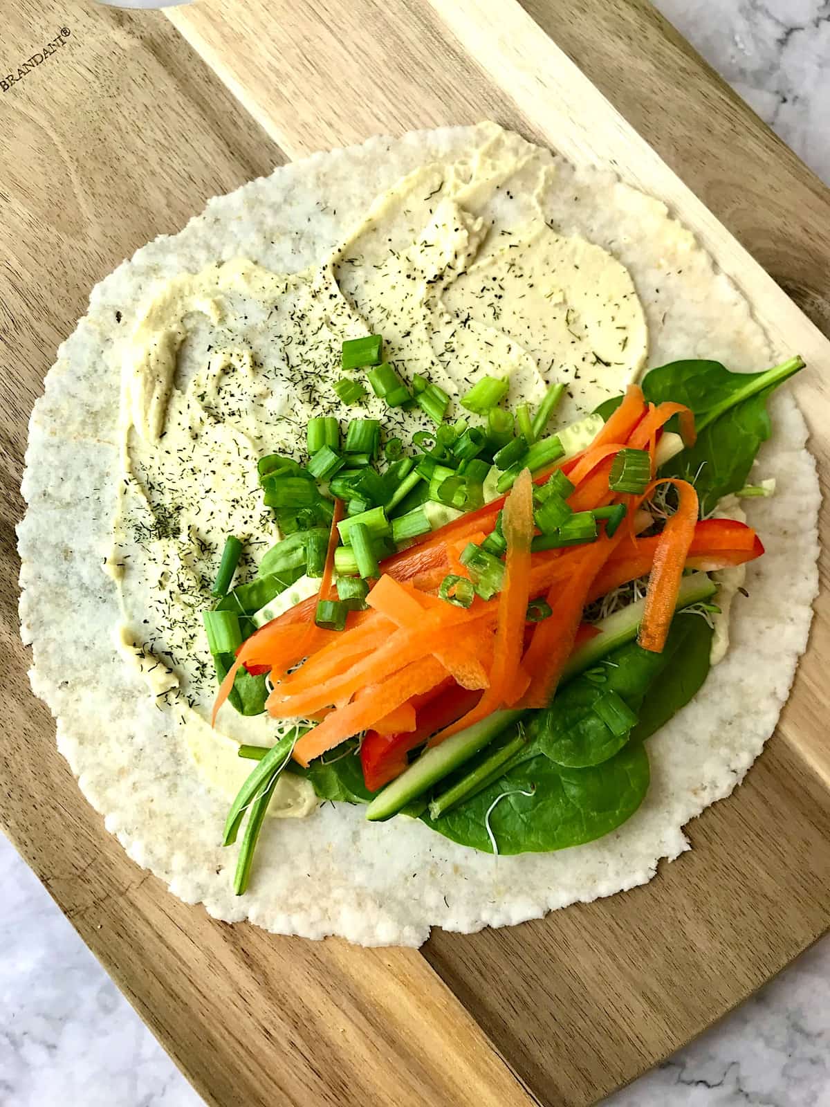 A tortilla topped with hummus and a variety of veggies.