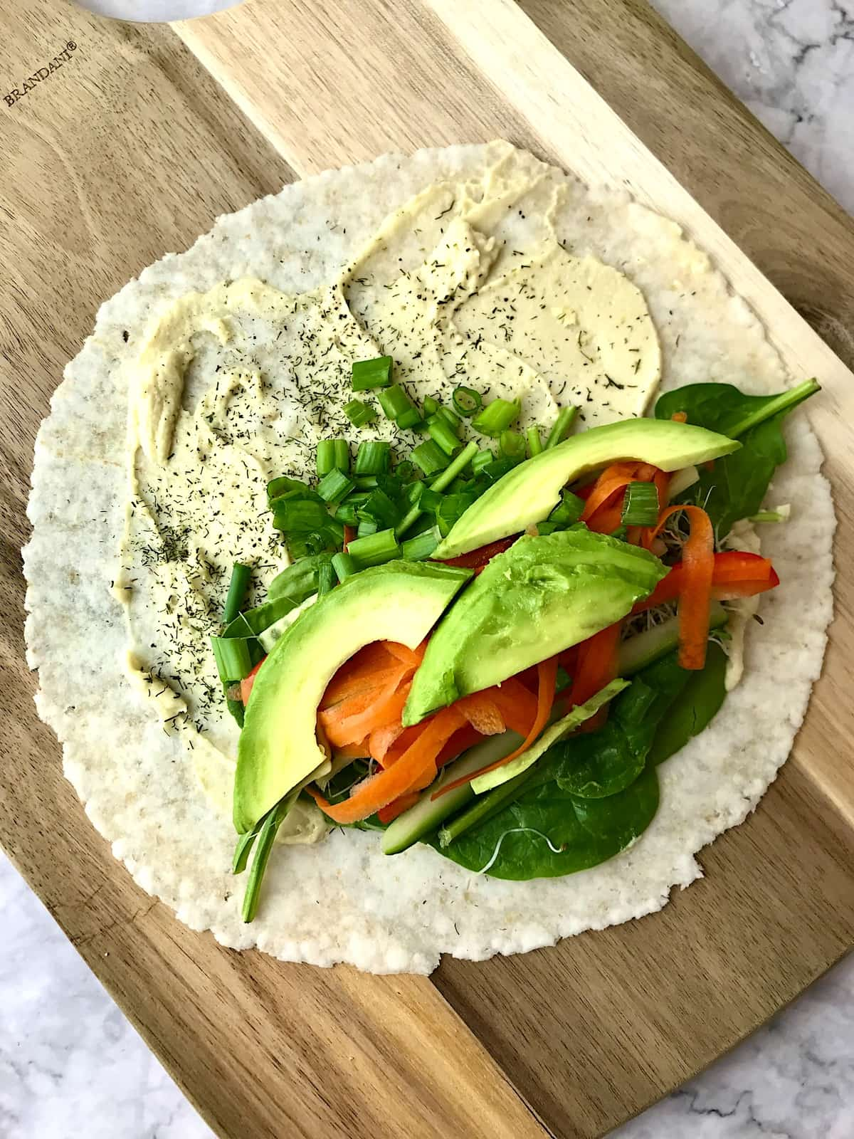 A tortilla topped with hummus, various veggies, and sliced avocado.