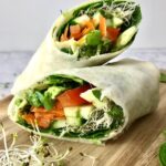 Two halves of a vegan hummus wrap full of vegetables.