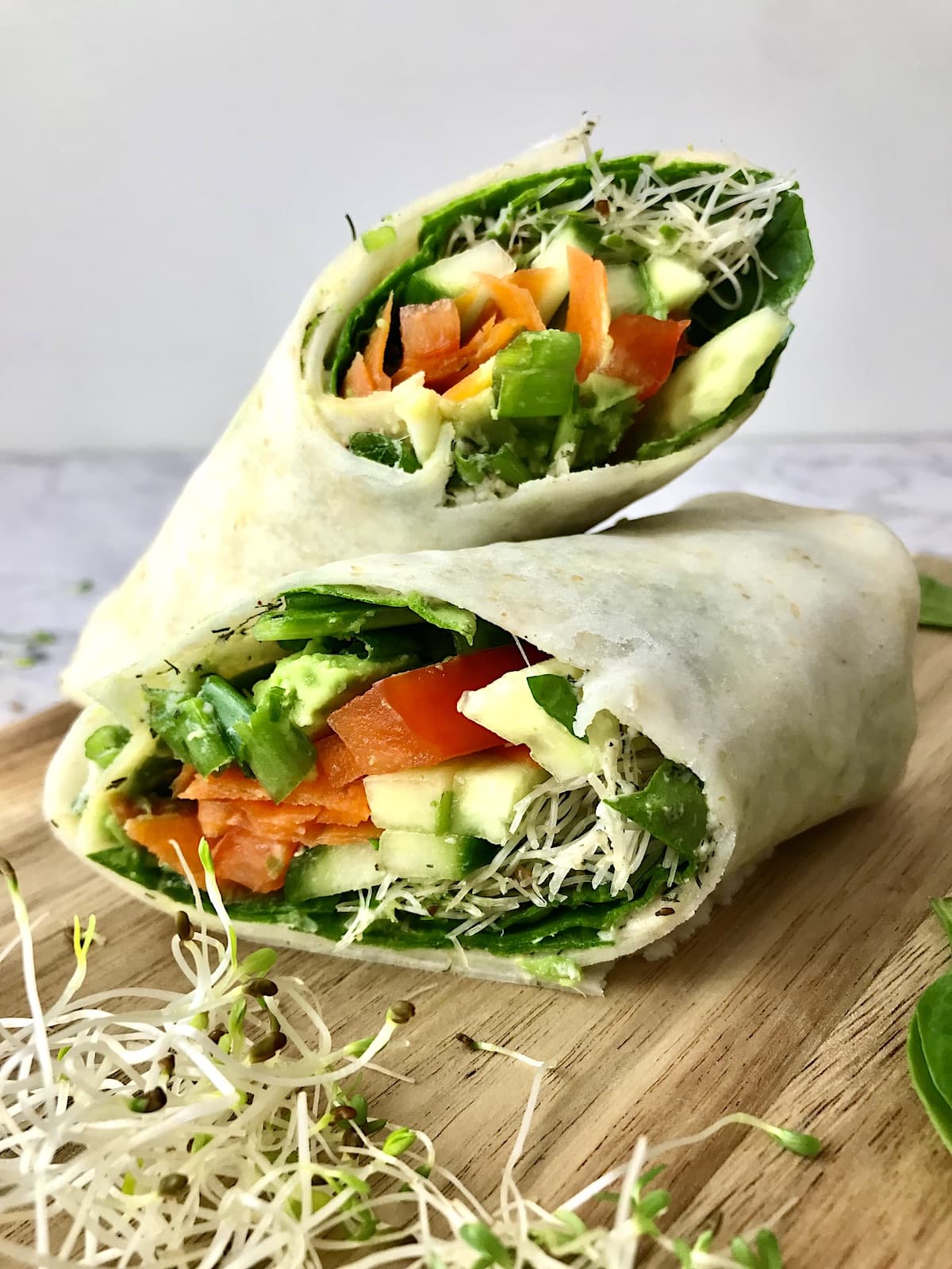 Two halves of a vegan hummus wrap full of vegetables.