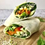 Two halves of a vegan hummus wrap full of vegetables.