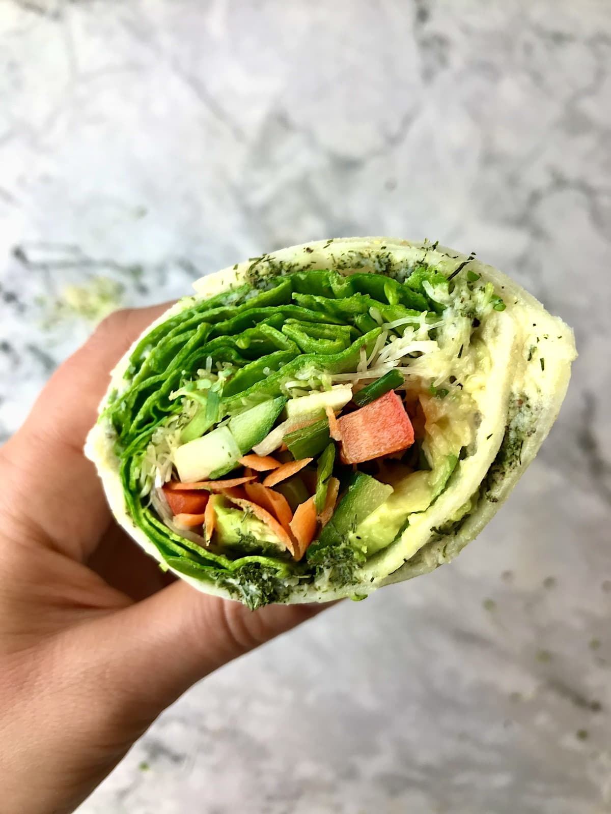 A hand holding half of a wrap filled with various vegetables.