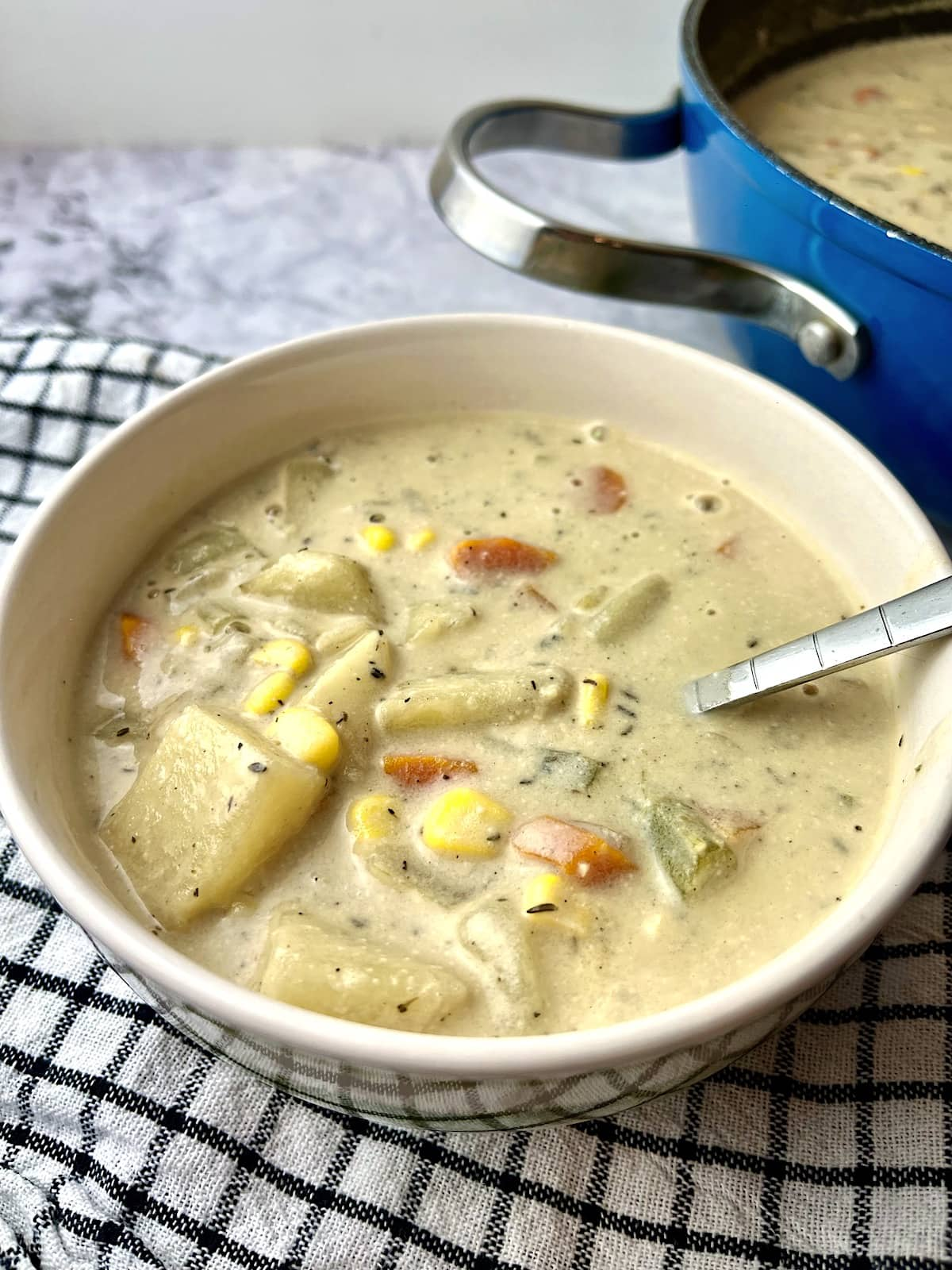 A bowl of vegan potato soup in front of a blue pot of more soup.