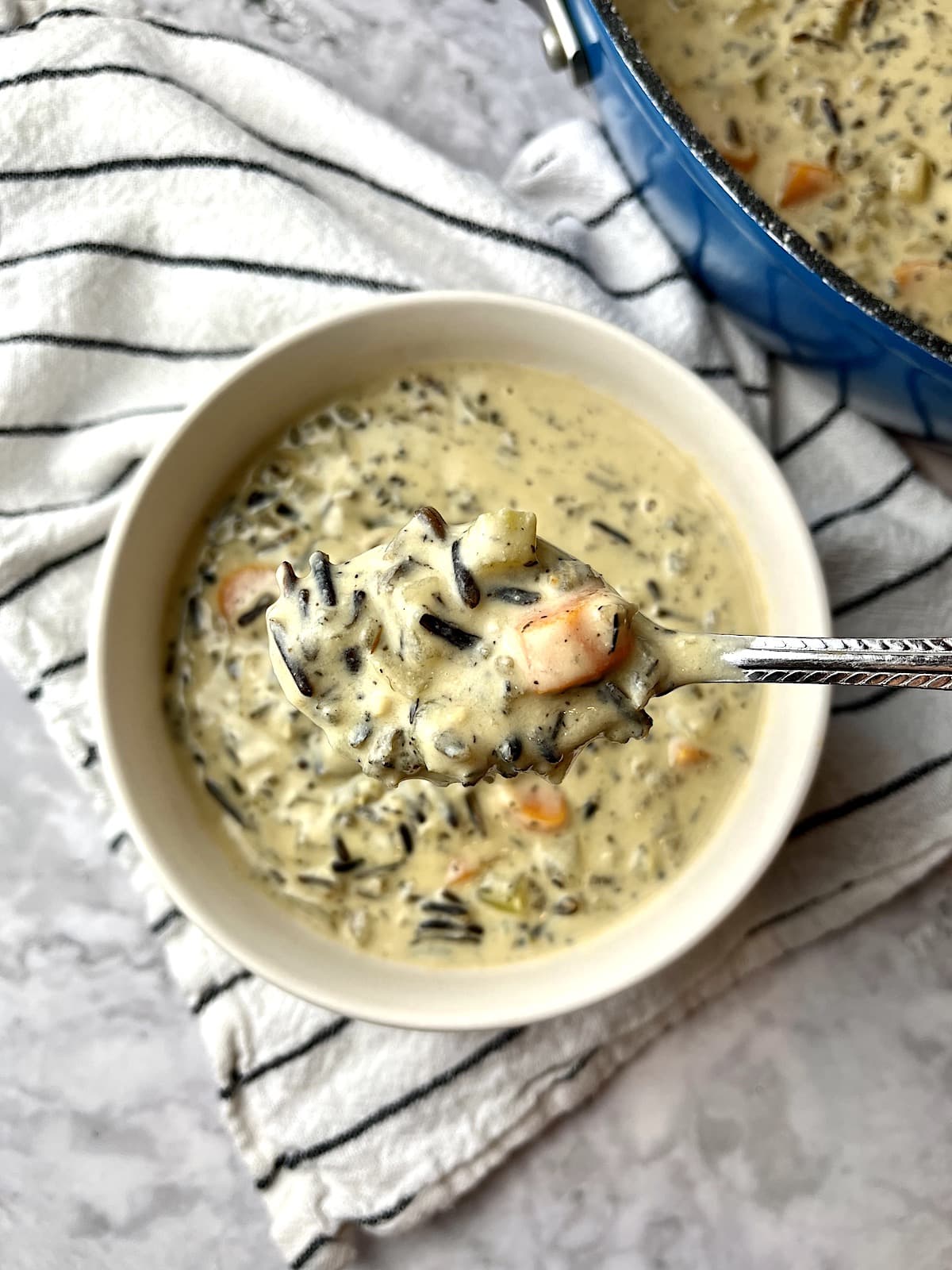 A spoonful of wild rice soup over a bowl of more soup, on a black and white striped towel.