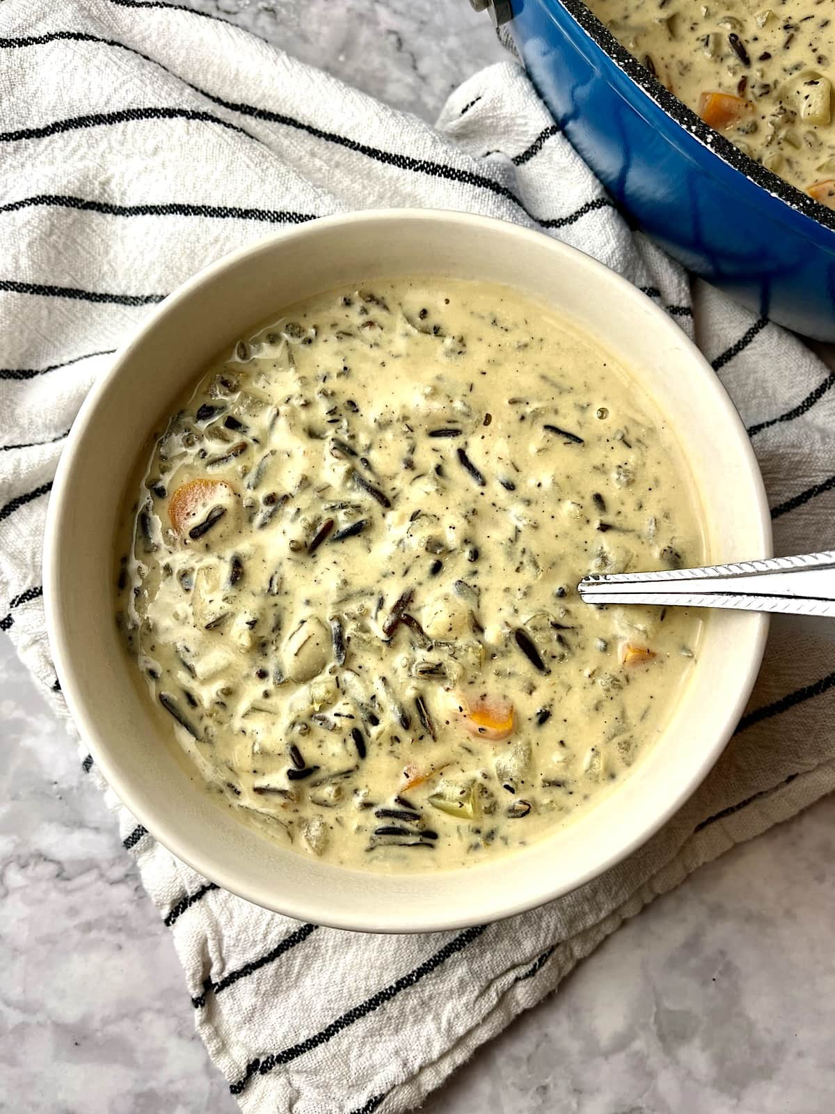 A bowl of vegan wild rice soup with a spoon in it, sitting on a black and white striped dish towel.