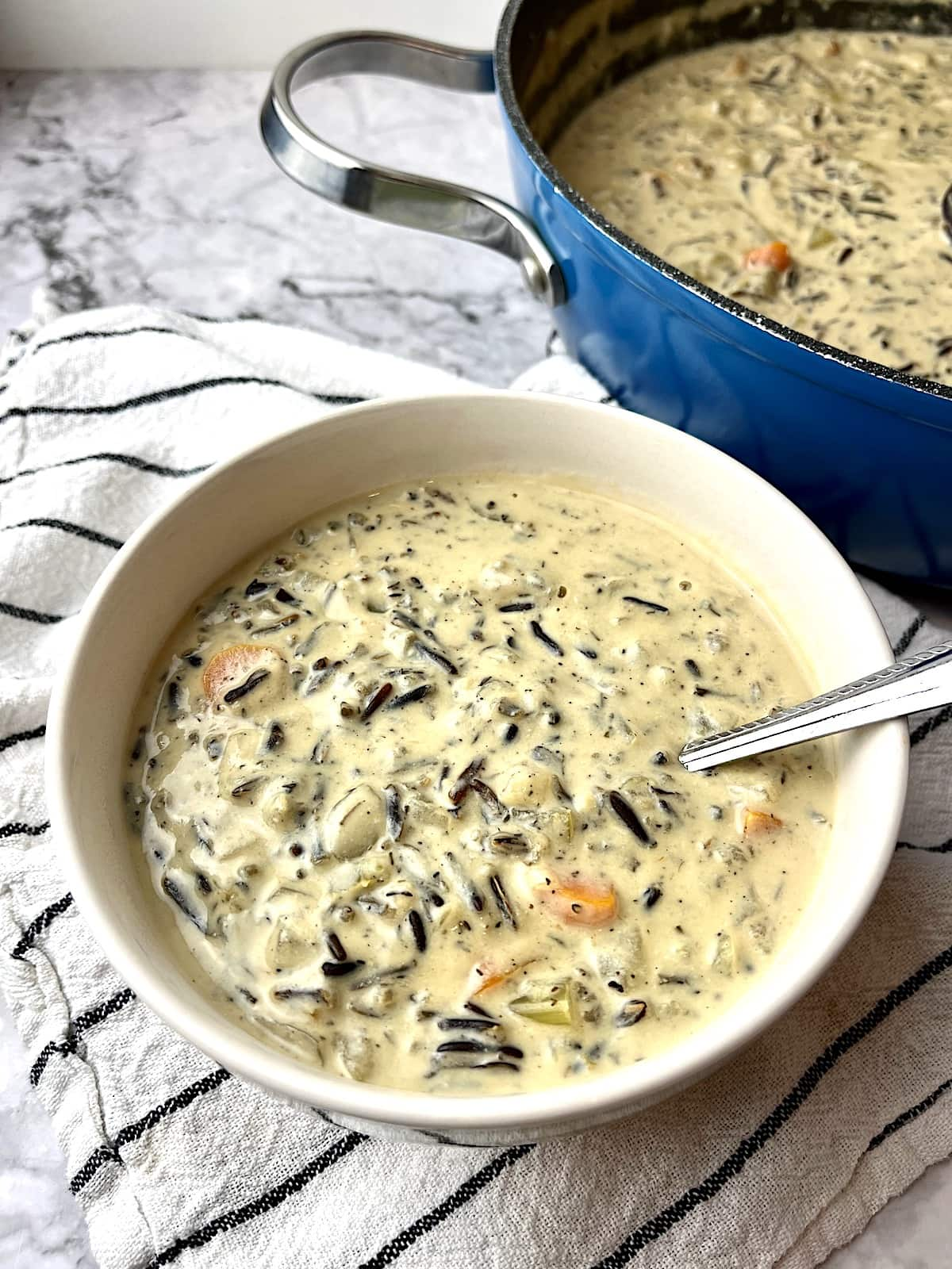 A bowl of vegan wild rice soup with a large pan of soup in the background.