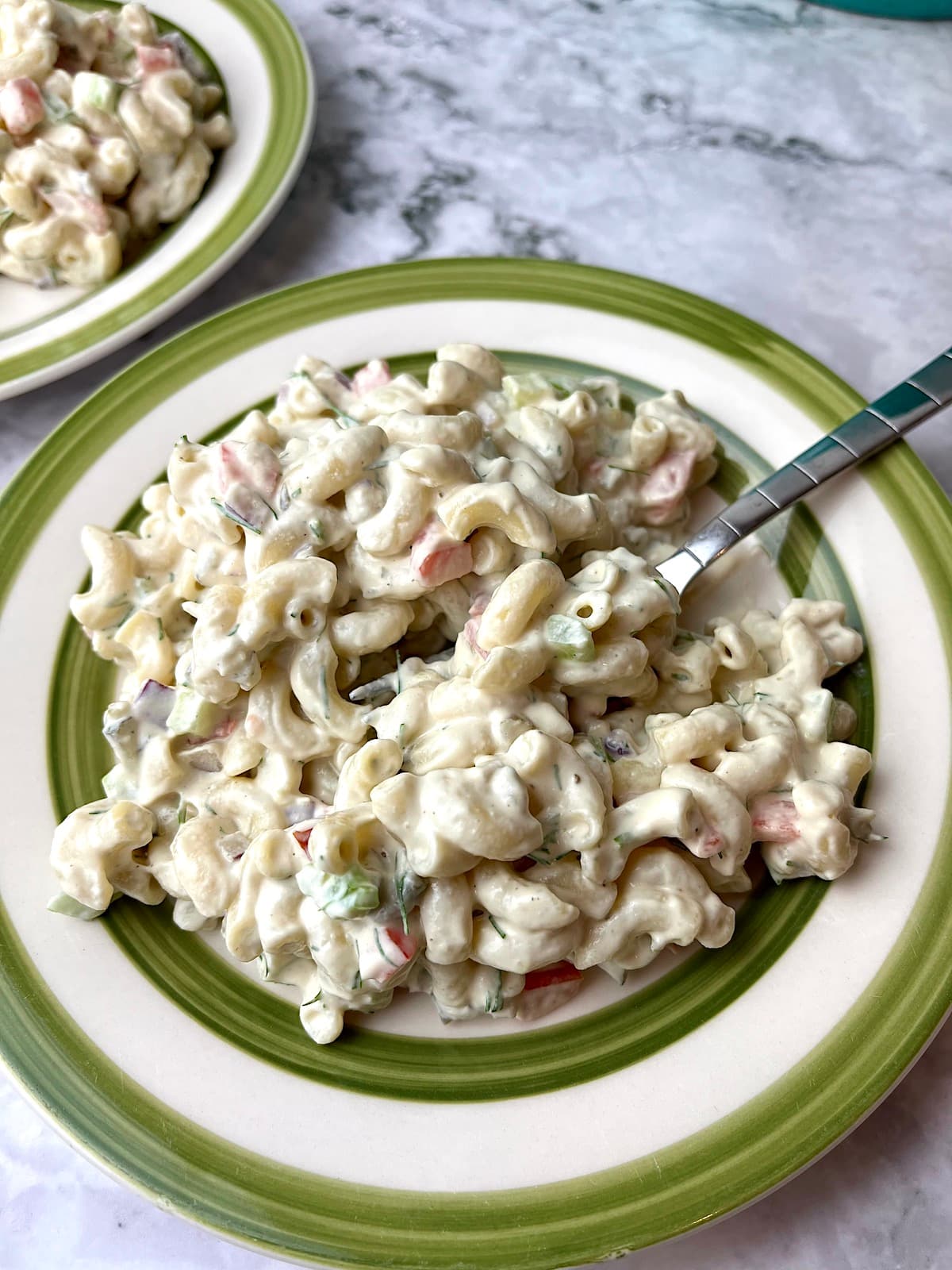 A plate of creamy macaroni salad with a fork in it.