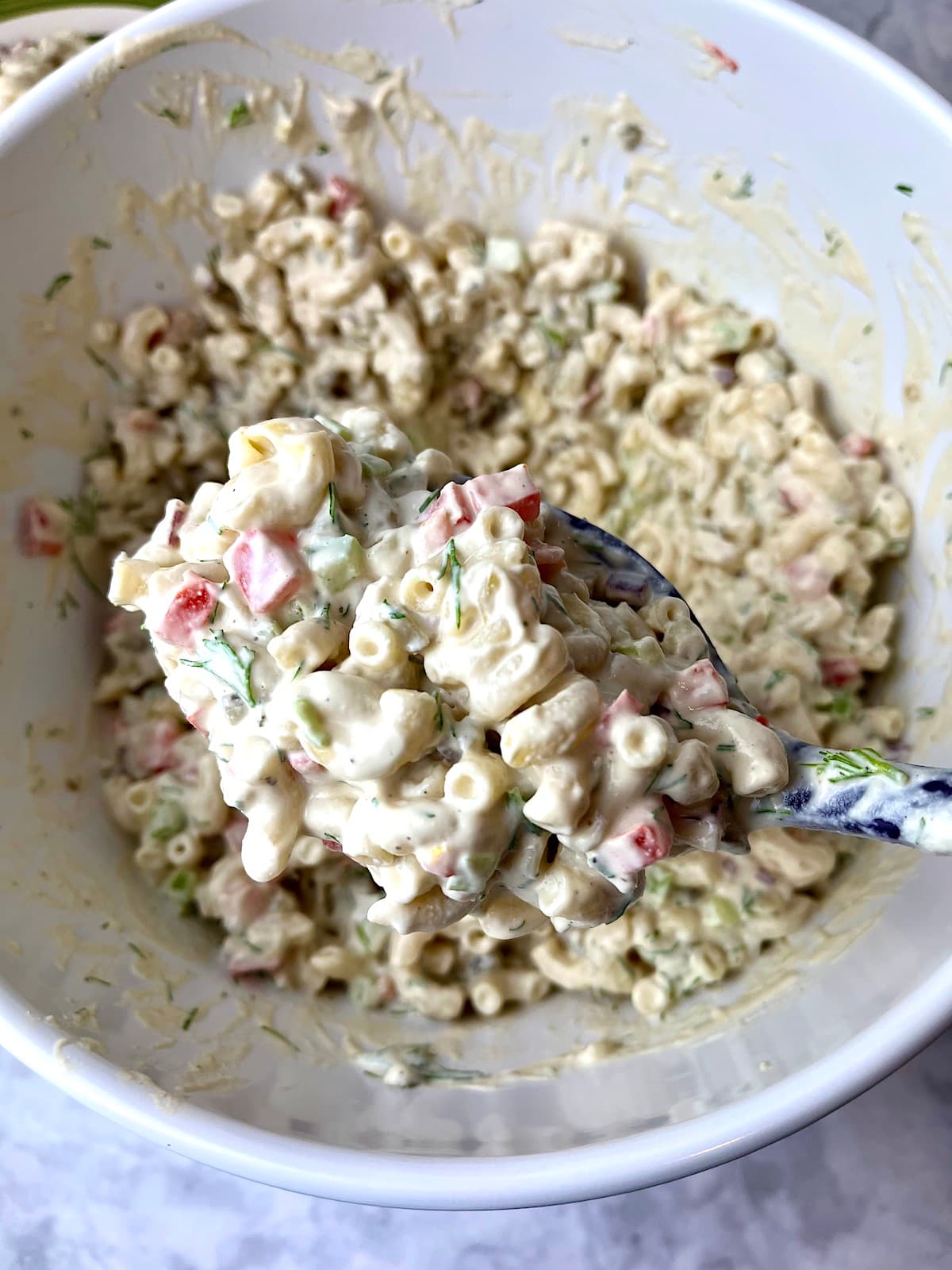 A spoonful of vegan macaroni salad over a bowl of more salad.