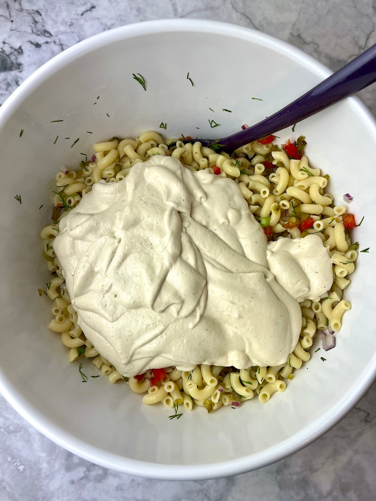 A bowl of macaroni salad ingredients topped with a thick creamy vegan dressing.