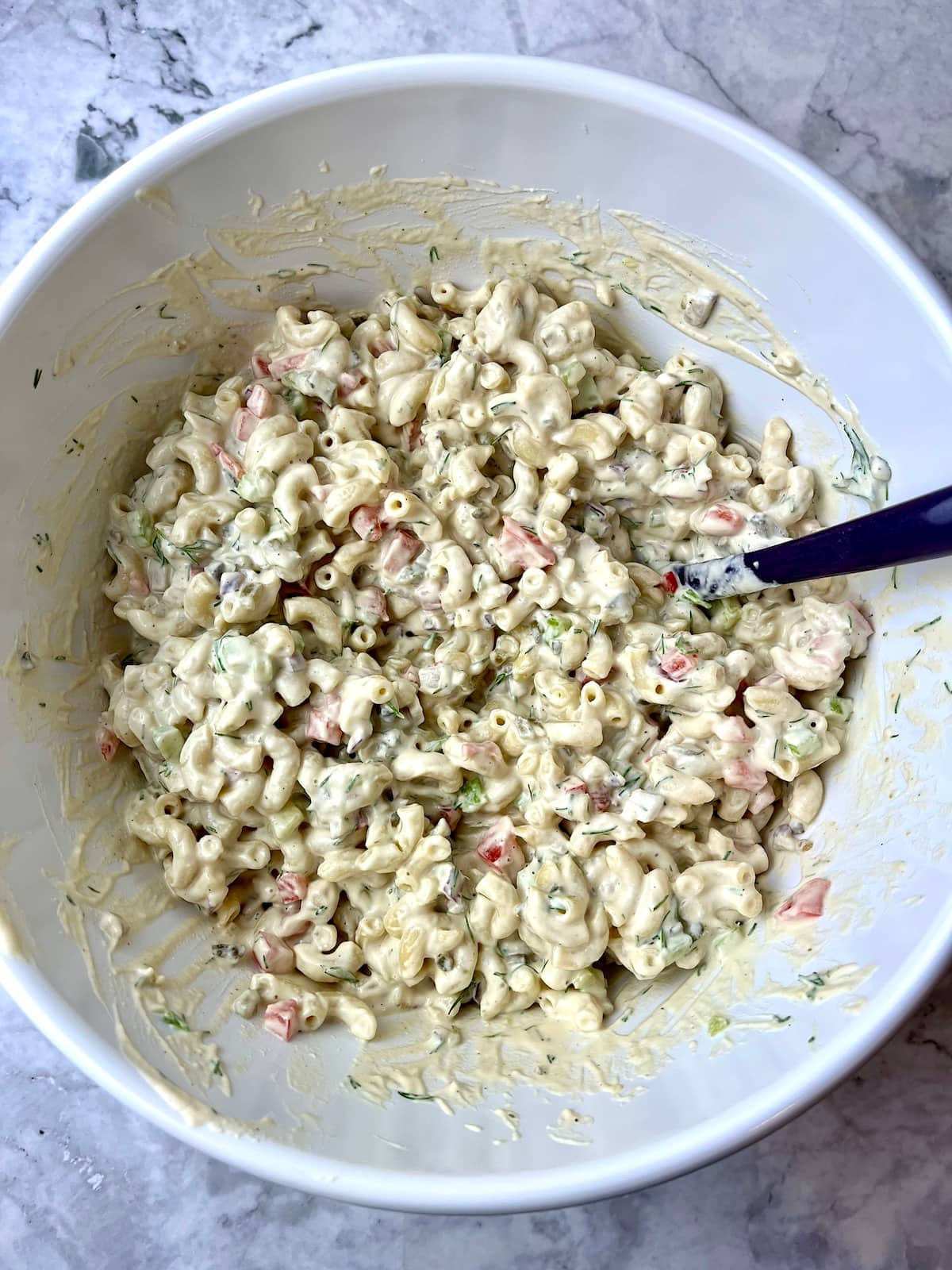 A large mixing bowl of macaroni salad with a serving spoon in it.