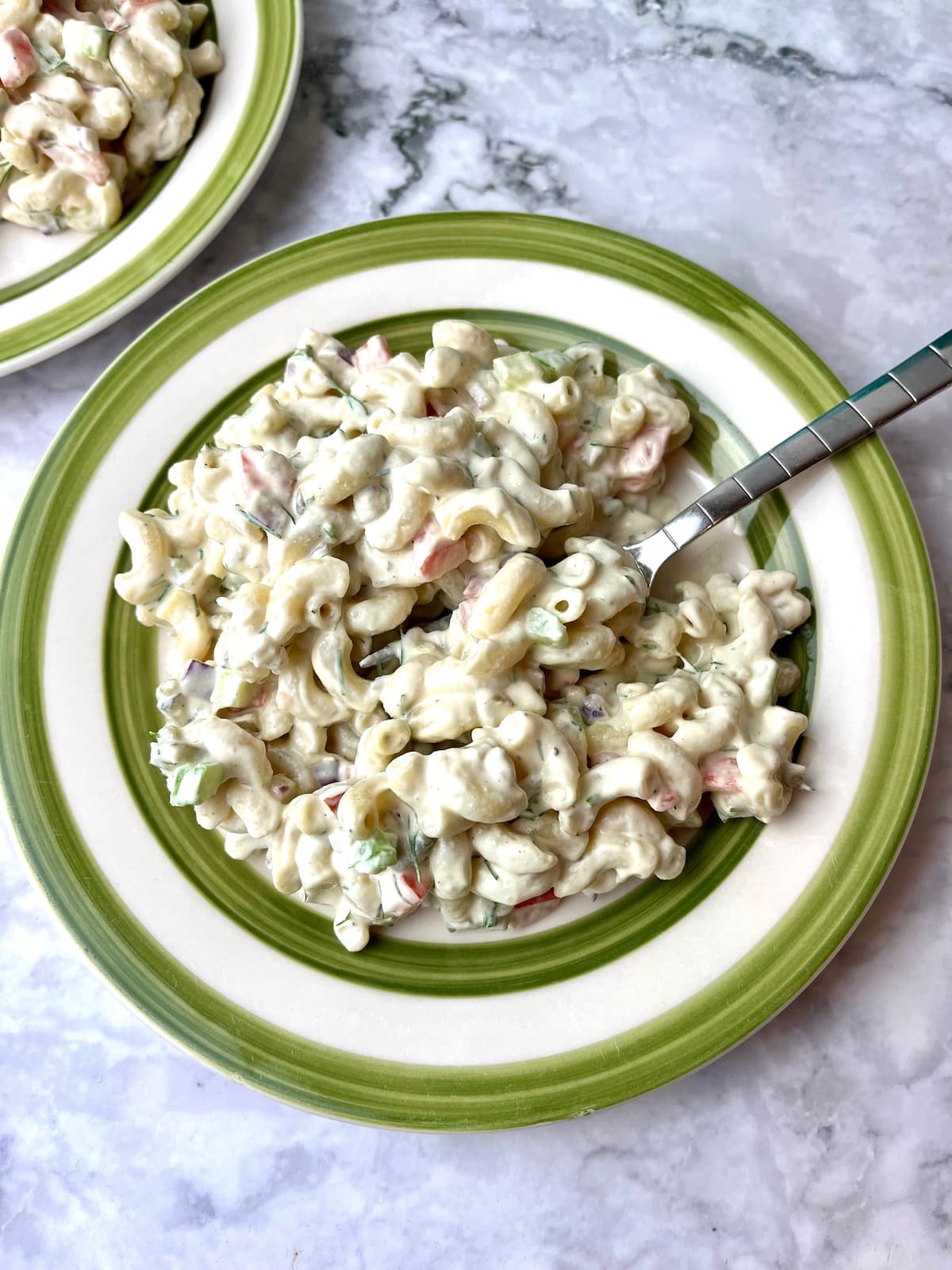 A plate of creamy macaroni salad with a fork in it.