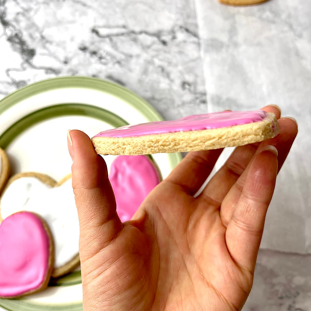 A hand holding a heart-shaped cookie with pink icing.